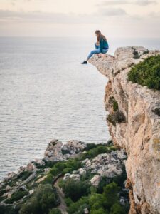 This captivating image features a woman sitting on the edge of a cliff overlooking the vast expanse of the ocean. The woman appears contemplative and serene, with her legs crossed and her hands resting on her knees. The ocean stretches out before her, with waves crashing against the rocks and a clear blue sky above. The image captures a sense of peace and calm, despite the raw power of the ocean. This image represents the transformative power of anxiety therapy in MN, where individuals can learn to manage their anxiety and find inner peace in the face of life's challenges.